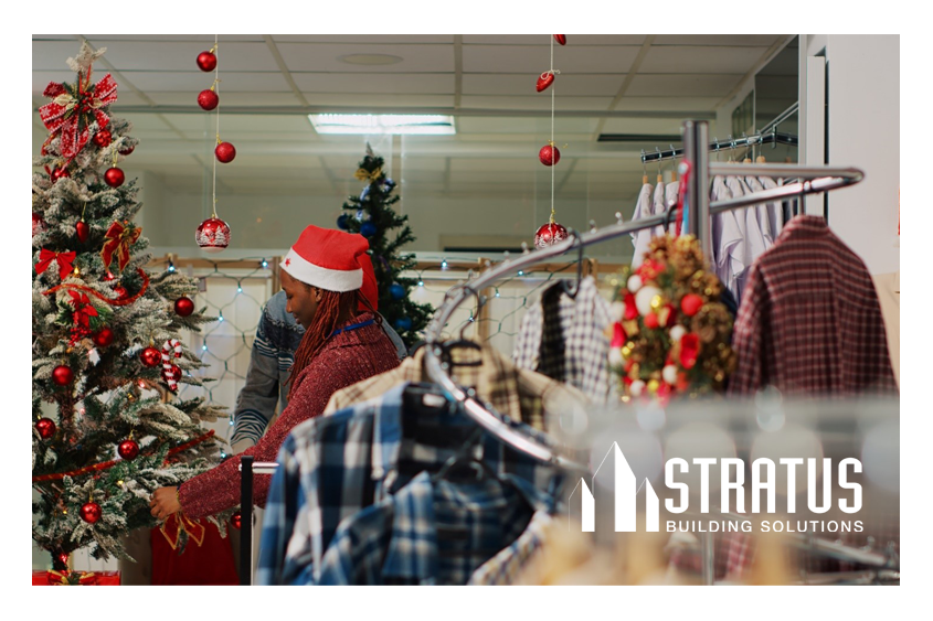 A rack of clothes in front a Christmas tree and a retail worker decorating a store for Christmas. 