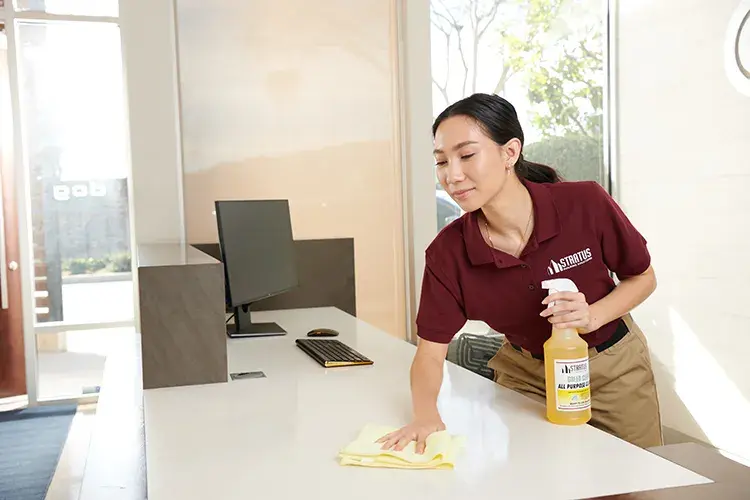 a woman cleaning the surface of a desk with a spray bottle in her hand